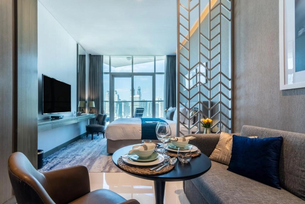 Modern studio apartment interior at Damac Maison Prive in Business Bay, Dubai, showing a well-equipped kitchenette, cozy sleeping area, and living space with large windows overlooking the city.
