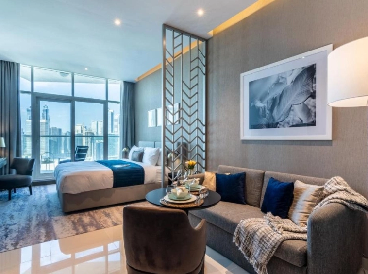 Modern studio apartment interior at Damac Maison Prive in Business Bay, Dubai, showing a well-equipped kitchenette, cozy sleeping area, and living space with large windows overlooking the city.