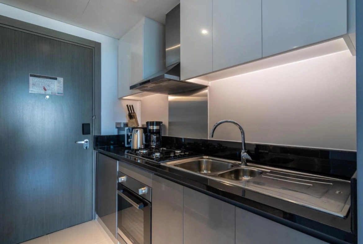 Modern studio apartment interior at Damac Maison Prive in Business Bay, Dubai, showing a well-equipped kitchenette, cozy sleeping area, and living space with large windows overlooking the city.