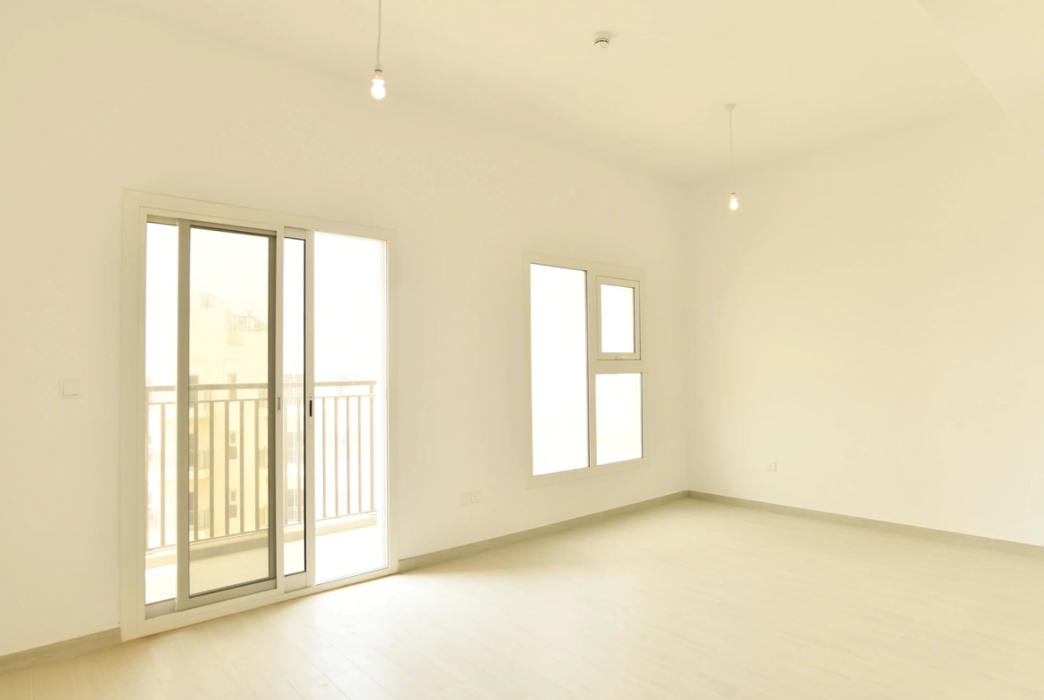 Living room with access to the balcony in a 2-bedroom apartment for sale in Al Rimth 13, Remraam, Dubai.